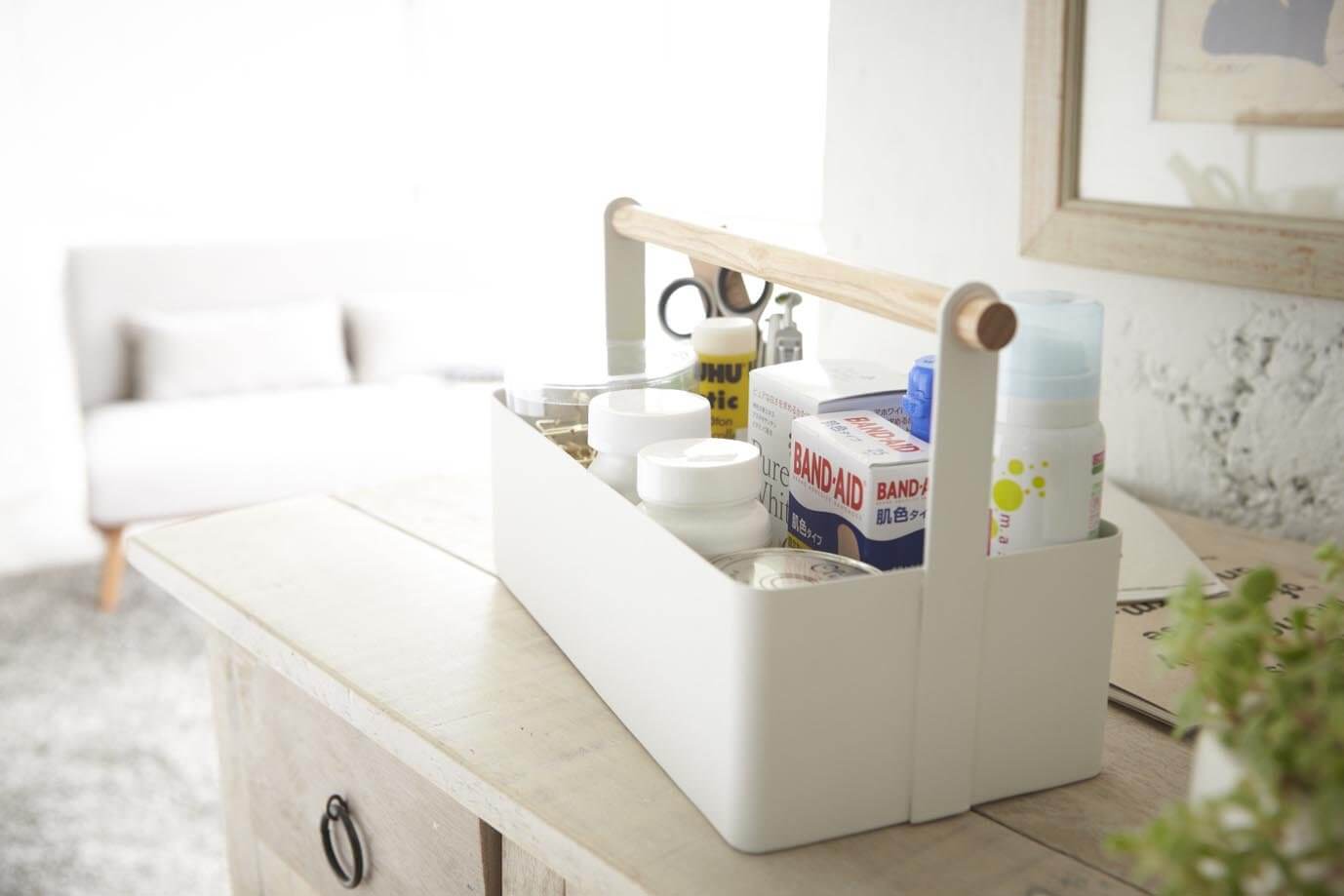 Rectangular white Yamazaki toolbox with wooden handle containing household items, sitting on dresser.