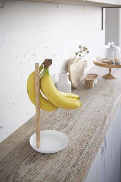 Yamazaki's wooden banana hanger with white accents sitting on a kitchen shelf
