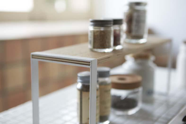 Spice jars on top of a Yamazaki wooden shelf riser in the kitchen.
