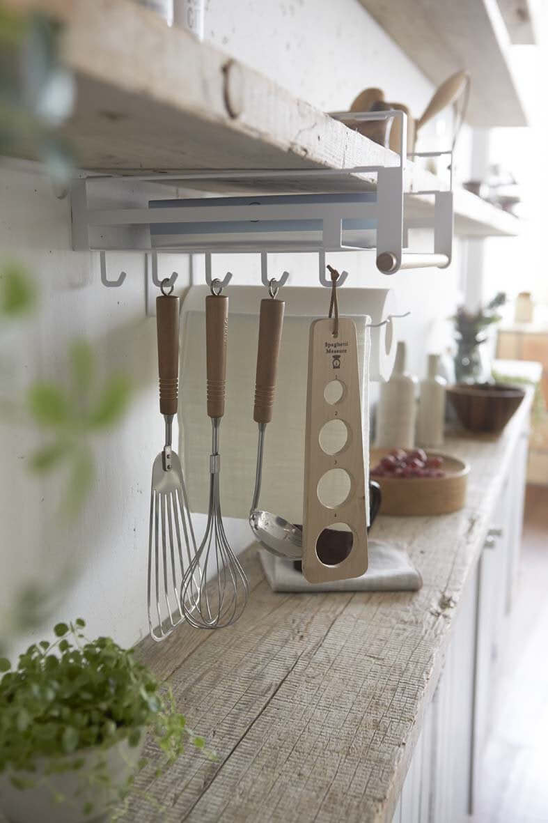 Yamazaki rack hanging from kitchen shelf holding paper towels and utensils.