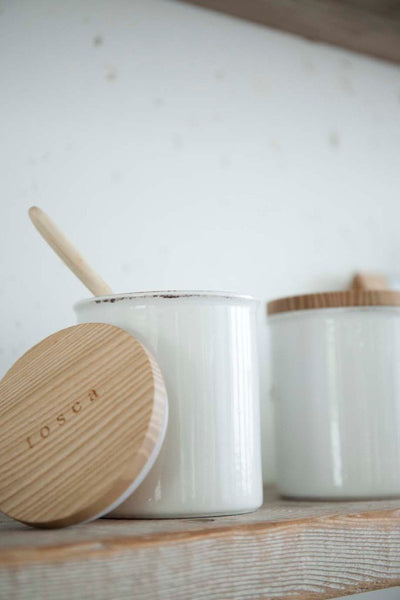 Two white Yamazaki ceramic canisters with wooden lids lined up on a kitchen shelf