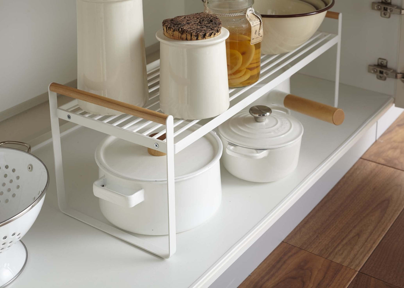 Side angled view of Yamazaki Wired Organizer Rack inside of a kitchen cabinet, stocked with mixing bowls and pots